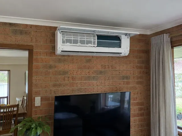 Clean split-system indoor unit with open front panel and visible filters on a brick wall in a home in Modbury