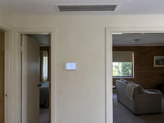 Ceiling return grille and wall controller in a beige hallway with adjoining rooms in Highbury